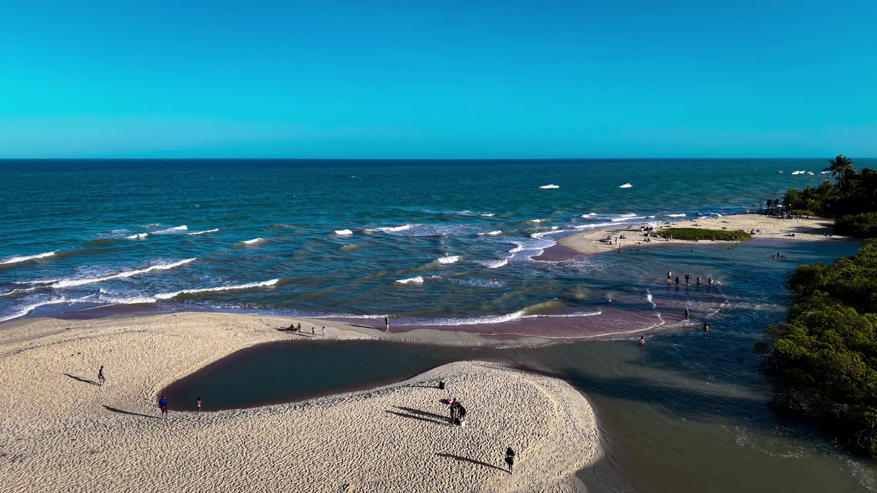 Banco de areia entre o rio e o mar, com pessoas caminhando no fim da tarde